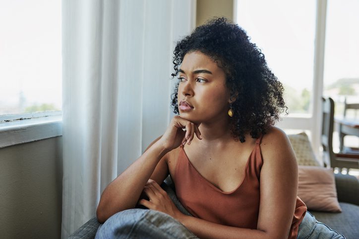 Shot of a young woman looking pensively out a window at home